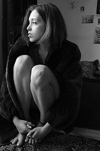 grayscale photo of woman wearing coat sitting with knees to chest thumbnail