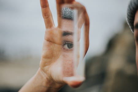person holding piece of glass reflecting person's eyes thumbnail