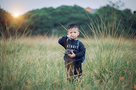 Boy Standing on Green Field Holding Black Camera thumbnail