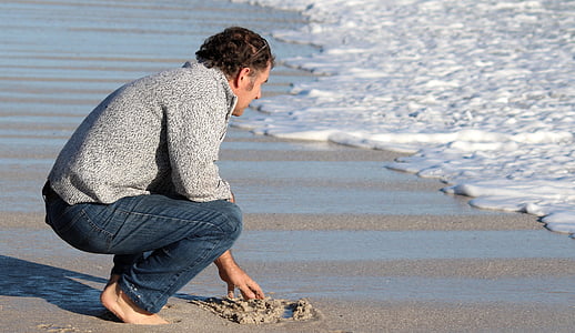 man holding brown sand in front body of water thumbnail