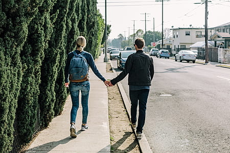 woman and man walking on sidewalk while holding hands thumbnail