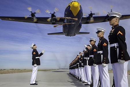 military personnel standing under flying airplane during daytime thumbnail