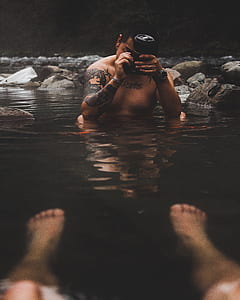 man taking photo of person's feet on calm water thumbnail