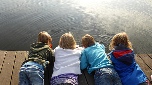 four toddlers in assorted-color jackets planking on brown wooden dock near water during daytime thumbnail