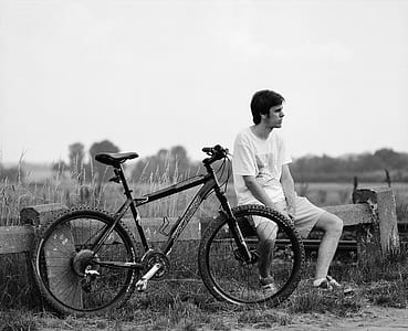 grayscale photography of man sitting beside his bike while looking at his left side thumbnail