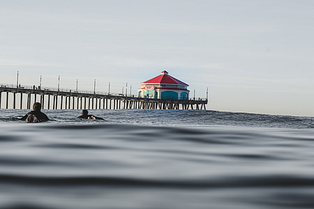 two people floating in sea near dock under grey sky thumbnail