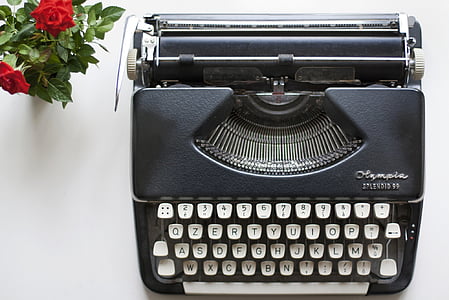 aerial view photography of black typewriter beside red roses thumbnail