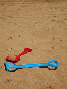 two red and teal plastic shovels on sand thumbnail