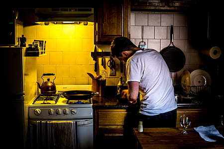 lowlight photography of man in white shirt standing in front of kitchen cabinet beside gas range oven thumbnail