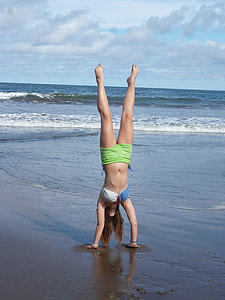 woman doing hand stand on shore near ocean during daytime thumbnail