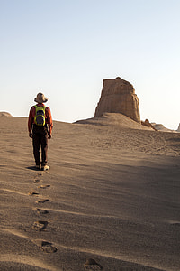 man walking on desert while fronting rock formation thumbnail