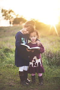 two girl's standing in green grass field reading book thumbnail