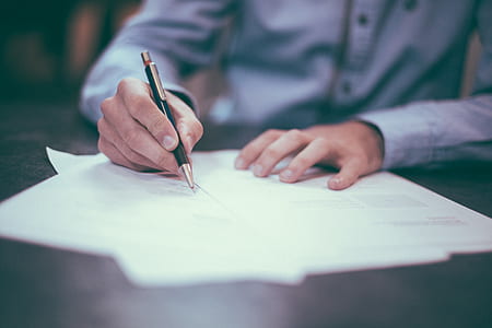 man wearing gray dress shirt writing on white printed paper thumbnail
