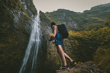 man in blue shorts wearing backpack near waterfall thumbnail