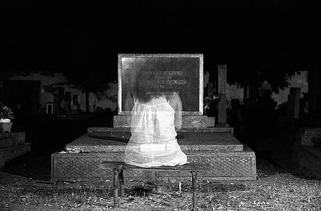 grayscale photo of woman in white dress sitting down in front of commemorative stone thumbnail