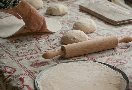 person holds dough near brown wooden rolling pin thumbnail