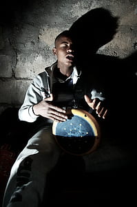 man playing drum while sitting beside wall thumbnail
