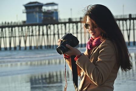Selective Focus Photography of Woman Holding Her Camera Near Seashore thumbnail