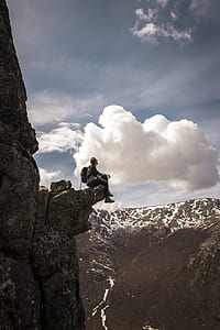 person wearing gray shirt seating on cliff during daytime thumbnail