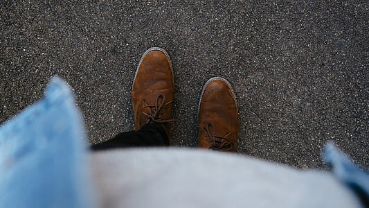person wearing brown dress shoes while standing on concrete pavement thumbnail