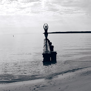 grayscale photo of woman standing on rock formation on sea thumbnail