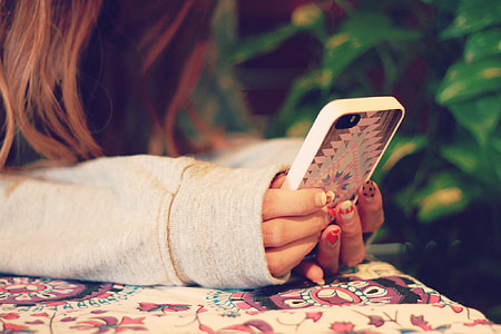 person in gray long-sleeve shirt holding iPhone with white and pink aztec print case thumbnail