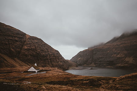 white concrete house near mountain and lake under gray skies thumbnail
