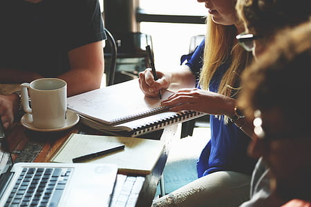 woman wears blue shirt holding pen writing near laptop thumbnail