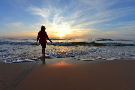 silhouette of woman standing on beach during golden hour thumbnail