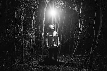 grayscale photo of man standing beside tree during nighttime thumbnail