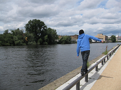 man walking while balancing on railing beside river at daytime thumbnail