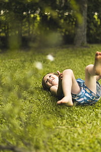 toddler lying on grass beside green trees thumbnail