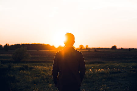 silhouette of man standing on grass field facing mountain range under golden hour thumbnail