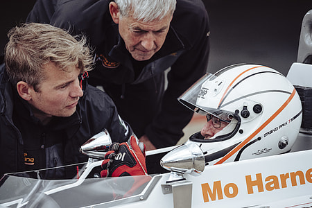 selective focus photography of two men standing beside man in white F1 race car at daytime thumbnail