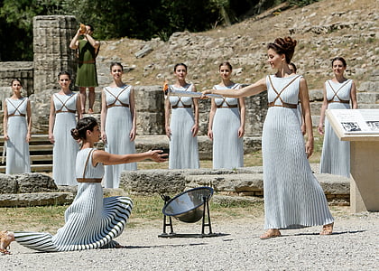 woman kneeling on ground while holding pot near woman standing surrounded by women thumbnail