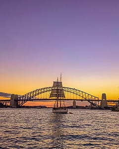 Sail Boat in Front of Bridge Under Orange Sunset thumbnail