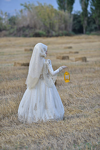 woman in white wedding abaya holding yellow kerosene lamp in brown field during daytime thumbnail