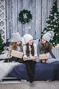three girls sitting on blue bed comforter holding brown gift boxes thumbnail