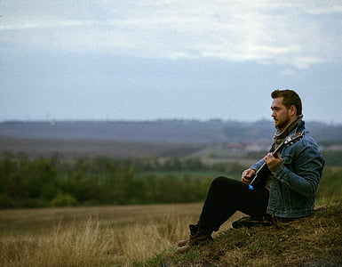 man in blue denim jacket playing guitar thumbnail