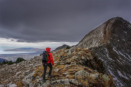 person wearing red hoodie standing on mountain near peak under grey cloudy sky thumbnail