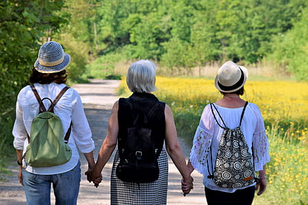 three women holding their hands while walking on road thumbnail