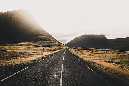 highway in between brown grass field leading to mountain under white clouds thumbnail
