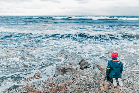 person kneeling on rock beside shore at daytime thumbnail