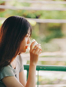 Selective Focus Photography of Woman Drinking Near Metal Fence thumbnail