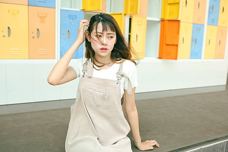 woman wearing khaki denim overalls sits on gray platform thumbnail