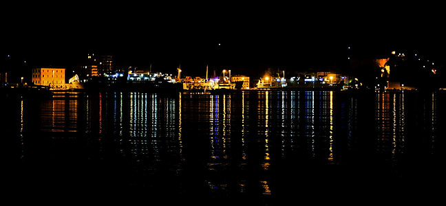 body of water near lighted buildings during nightime thumbnail