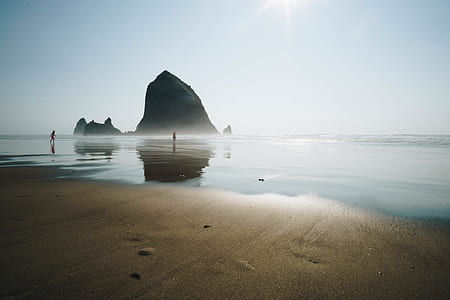 two person on seashore in the distance of rock under white sky thumbnail