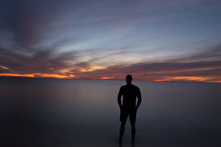 silhouette photo of person standing facing body of water thumbnail