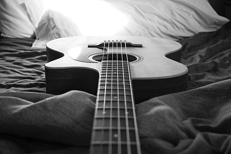 greyscale photo of acoustic guitar on bed thumbnail