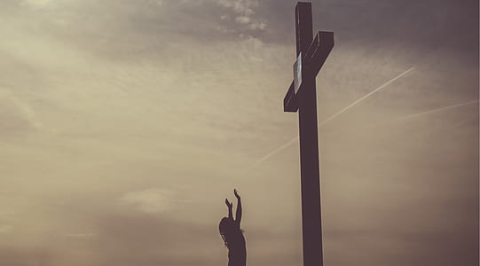 silhouette photography of person standing in front of cross thumbnail